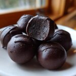 A stack of decadent, dark chocolate-coated Oreo balls, one cut open to show the dense filling.