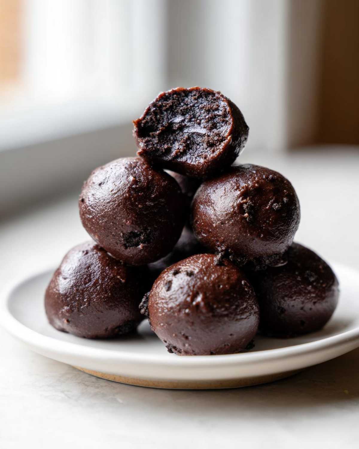 A stack of rich, dark chocolate Oreo balls, with one on top bitten open to show the dense interior.