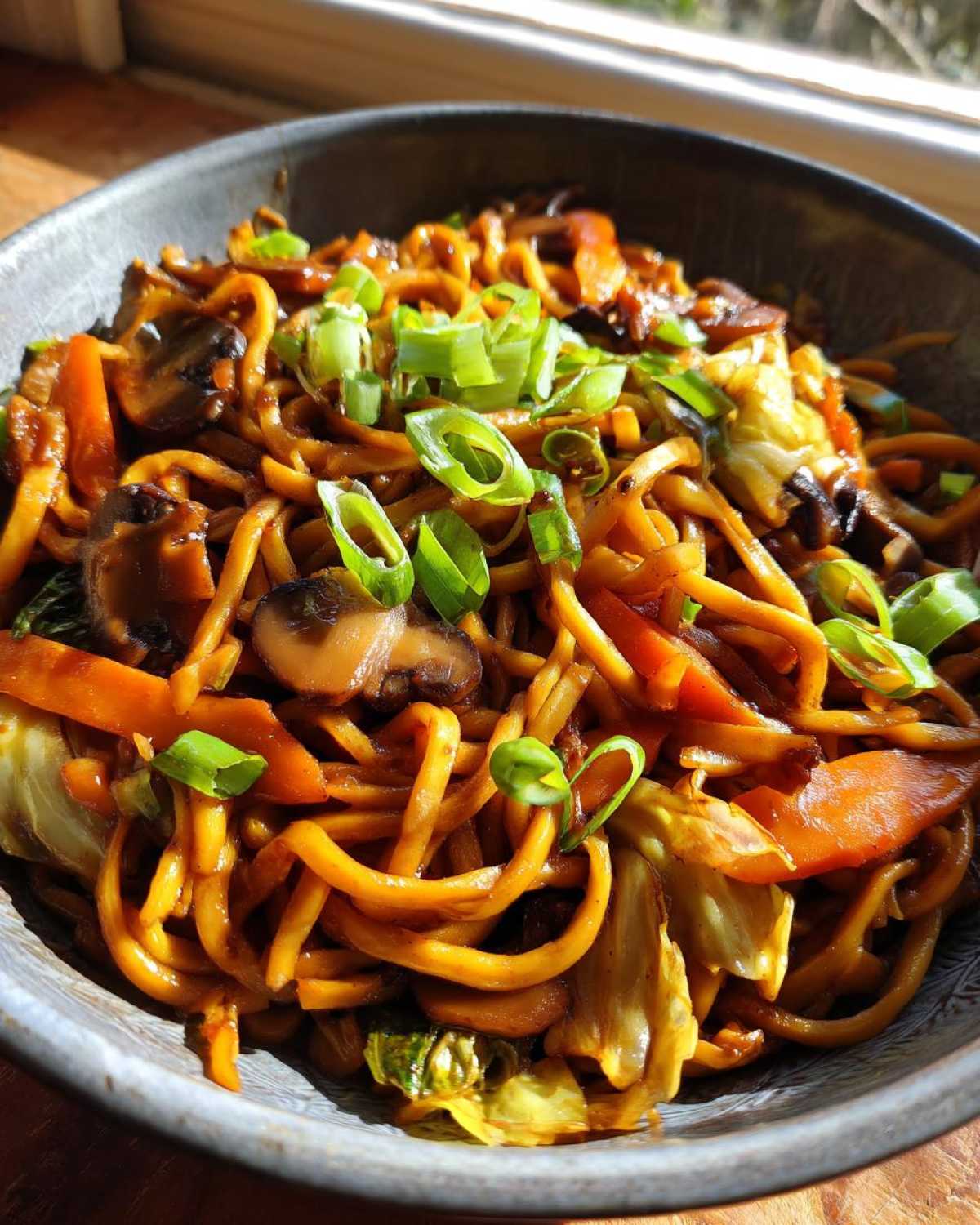 Close-up of savory fried noodles mixed with mushrooms and cabbage, topped with fresh green onions.