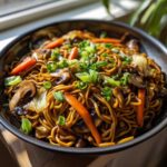 A close-up bowl of savory fried noodles mixed with sliced mushrooms, carrots, and topped with fresh green onions.