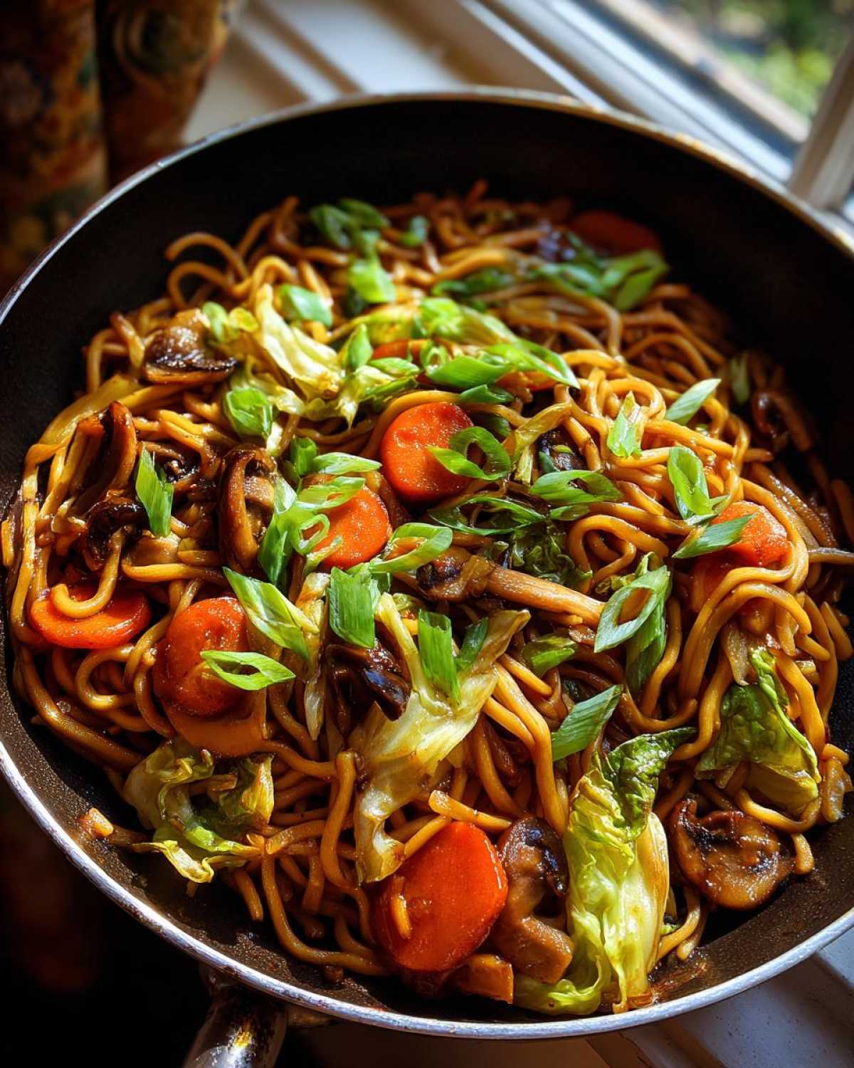 Close-up of savory fried noodles tossed with bright carrots, mushrooms, and cabbage, topped with green onions.