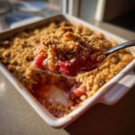 A spoonful of warm rhubarb crisp, showing juicy fruit filling and a golden, crunchy oat topping.