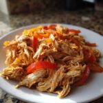 Shredded, seasoned chicken mixed with sliced red and orange peppers, ready for crockpot chicken fajitas.
