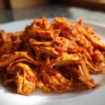Close-up of richly sauced, shredded chicken tinga piled high on a white plate.