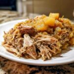 Close-up of tender, shredded pork and sauerkraut topped with chunks of cooked apple.