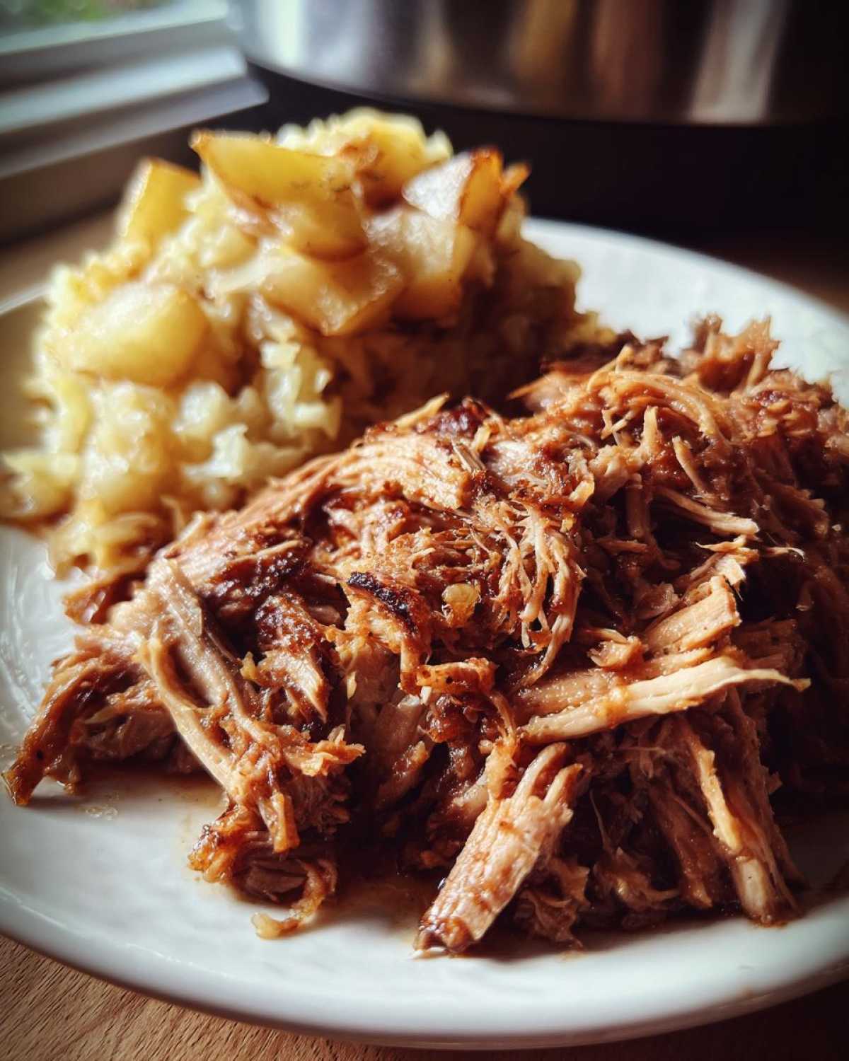 Close-up of shredded pork and sauerkraut served on a white plate next to a side of cooked apples.
