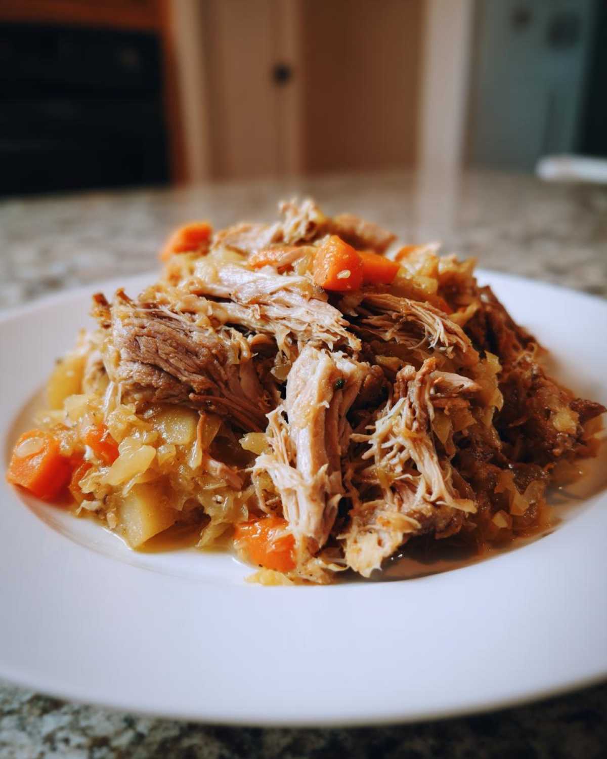 A close-up of shredded pork and sauerkraut mixed with carrots served on a white plate, highlighting the amazing pork and sauerkraut recipe.