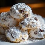 A close-up stack of soft cannoli cookies heavily dusted with powdered sugar and containing visible raisins.
