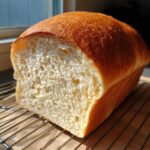 A freshly baked loaf of soft condensed milk bread, sliced to show the fluffy interior, cooling on a wire rack.