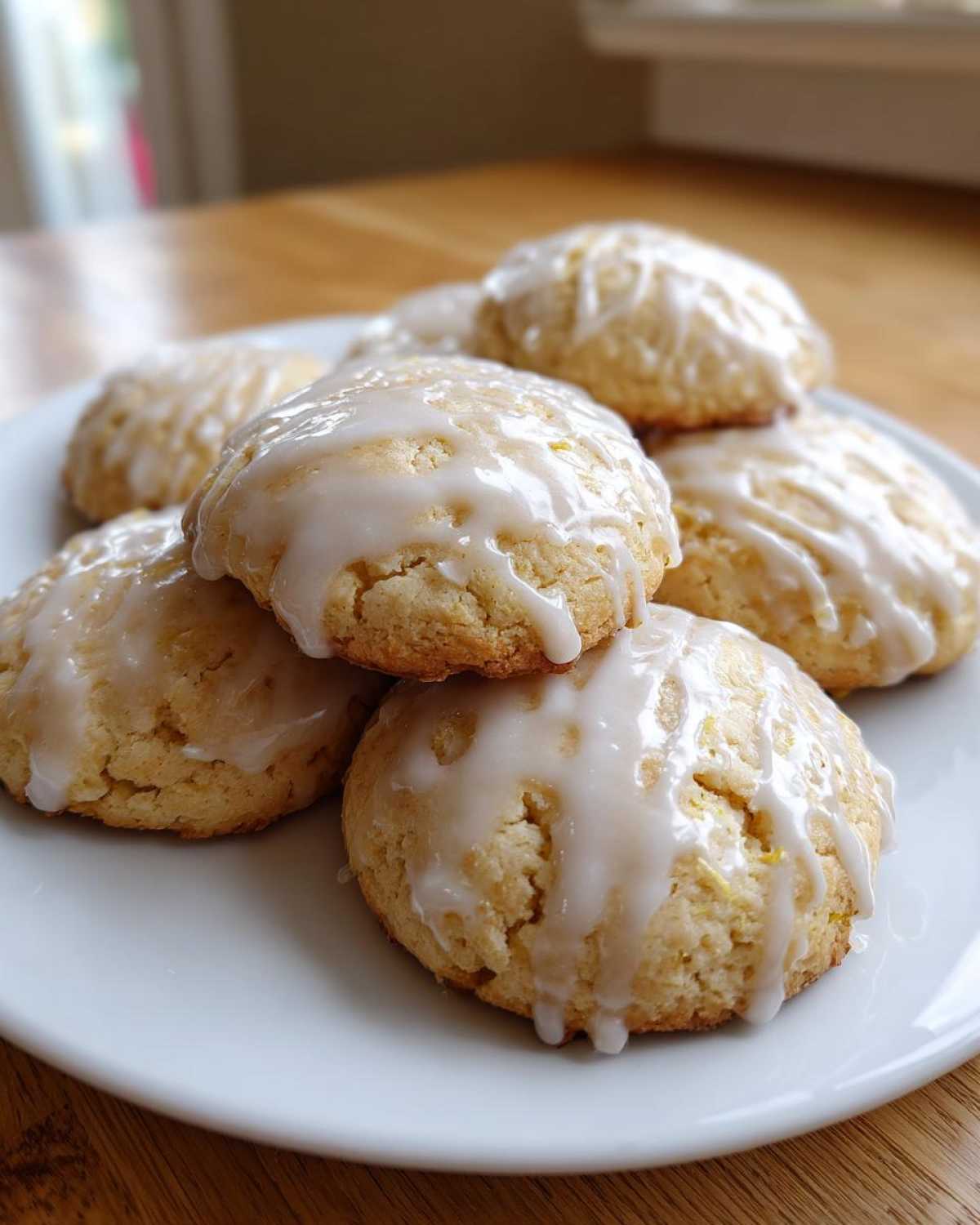 A close-up of several soft ricotta cookies piled on a white plate, drizzled generously with white glaze.