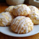 A plate of soft ricotta cookies topped with a thick white lemon glaze and lemon zest.