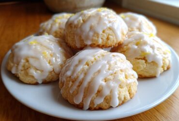 A plate of soft ricotta cookies topped with a thick white lemon glaze and lemon zest.