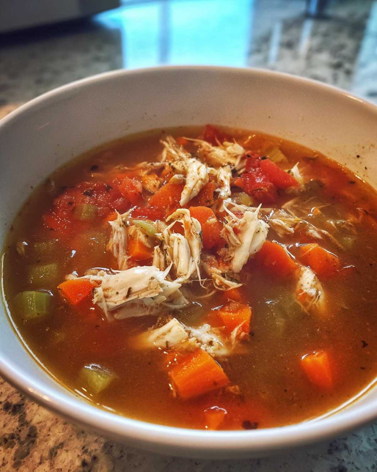 Close-up of a hearty bowl of soup containing shredded meat, diced carrots, celery, and tomatoes, despite the article being about maryland crab soup.
