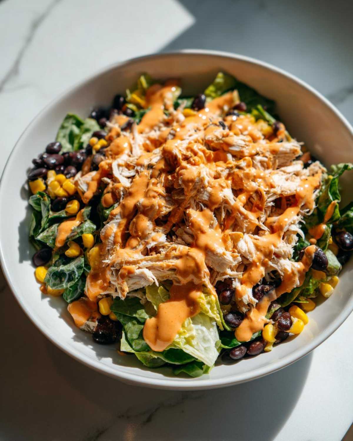 A vibrant bowl of southwest chicken salad featuring shredded chicken, black beans, corn, and a creamy orange dressing over greens.