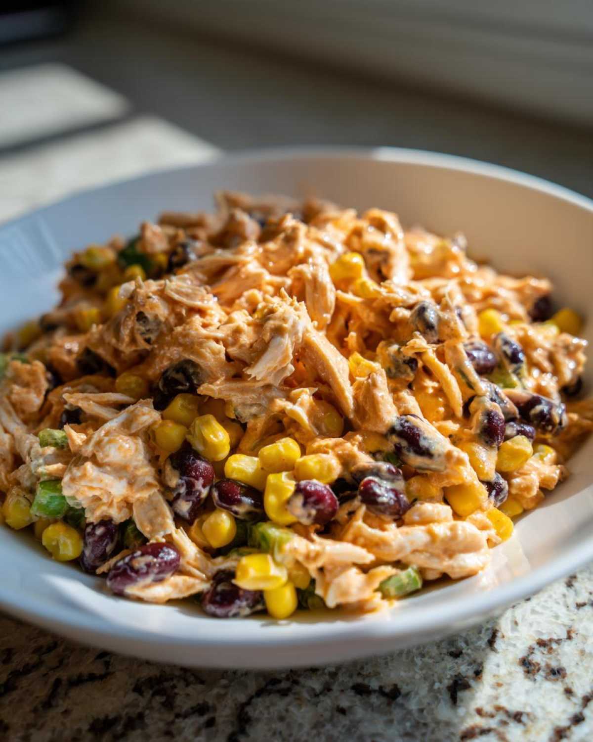 A close-up view of creamy southwest chicken salad featuring shredded chicken, corn, and black beans in a white bowl.