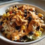 A close-up of a bowl of Southwest chicken salad topped with creamy orange dressing, black beans, and corn.