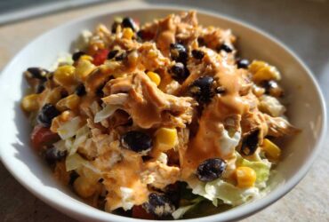 A close-up of a bowl of Southwest chicken salad topped with creamy orange dressing, black beans, and corn.