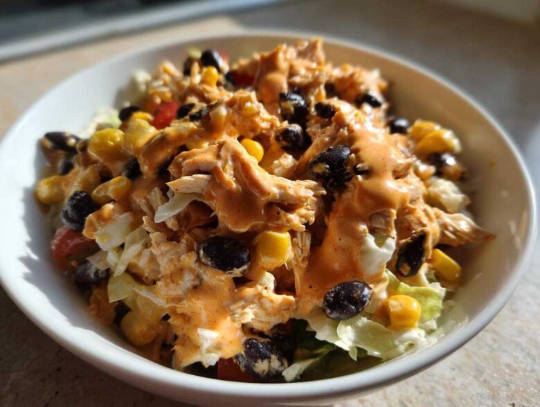 A close-up of a bowl of Southwest chicken salad topped with creamy orange dressing, black beans, and corn.