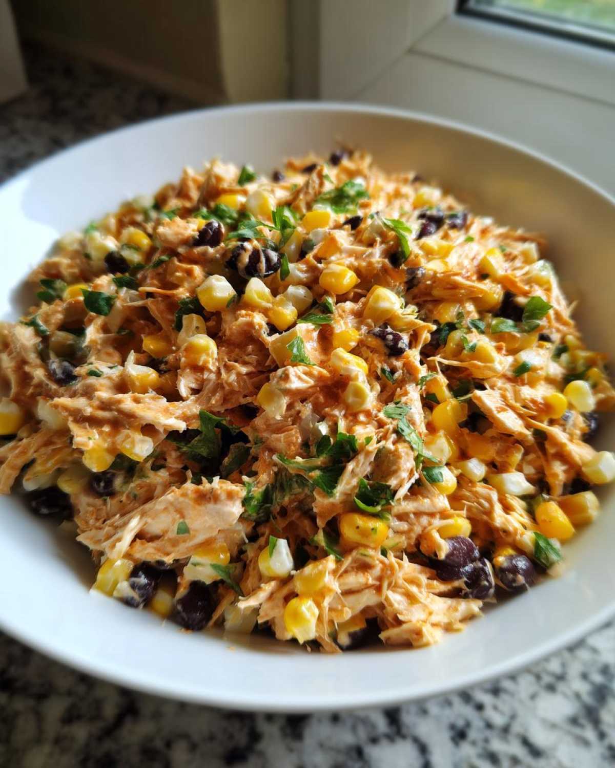 A close-up view of creamy Southwest chicken salad mixed with corn and black beans, garnished with parsley.