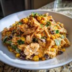 A close-up of creamy Southwest chicken salad mixed with black beans and corn, served in a white bowl.