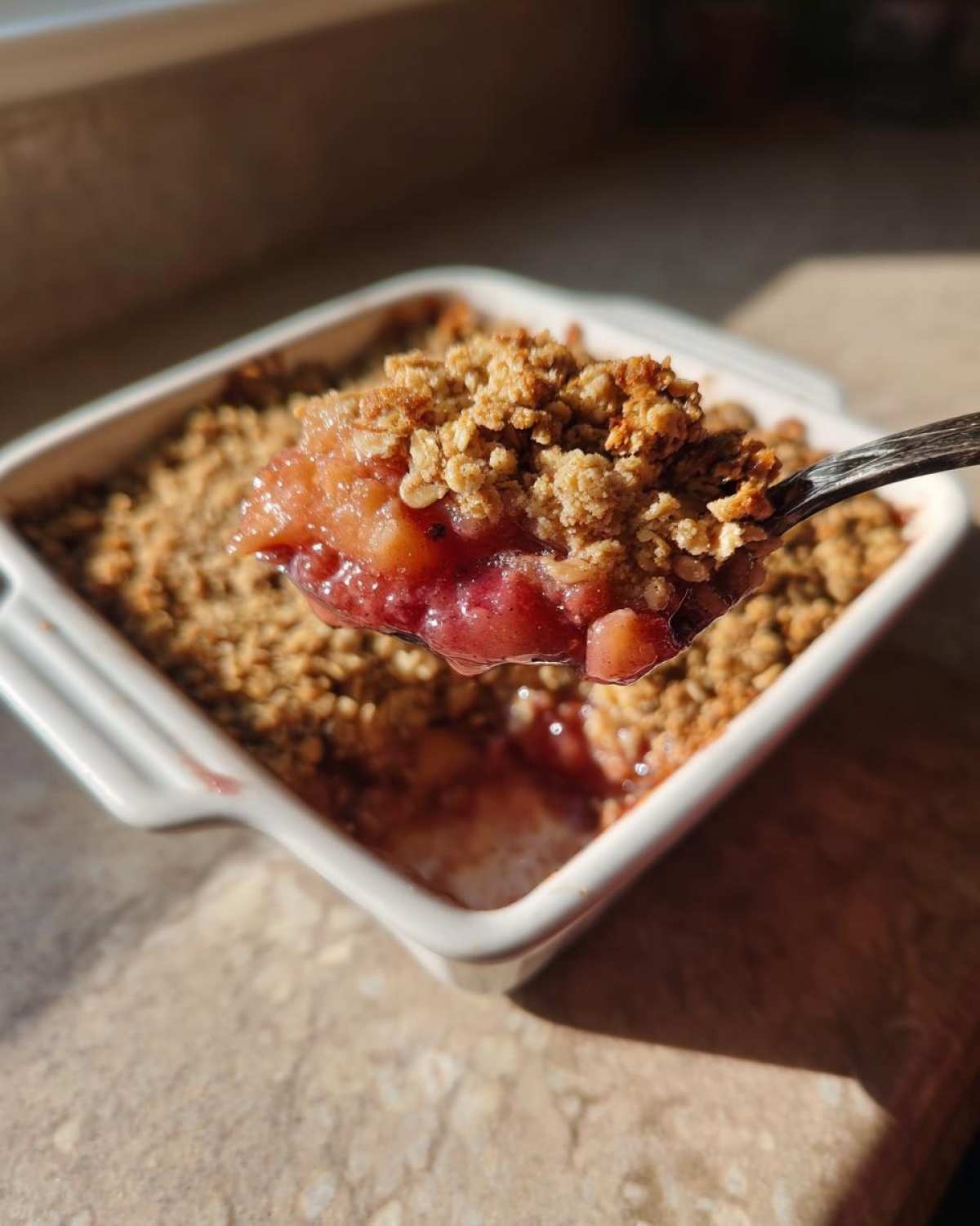 A spoonful of warm, bubbly rhubarb crisp being lifted out of a white baking dish.