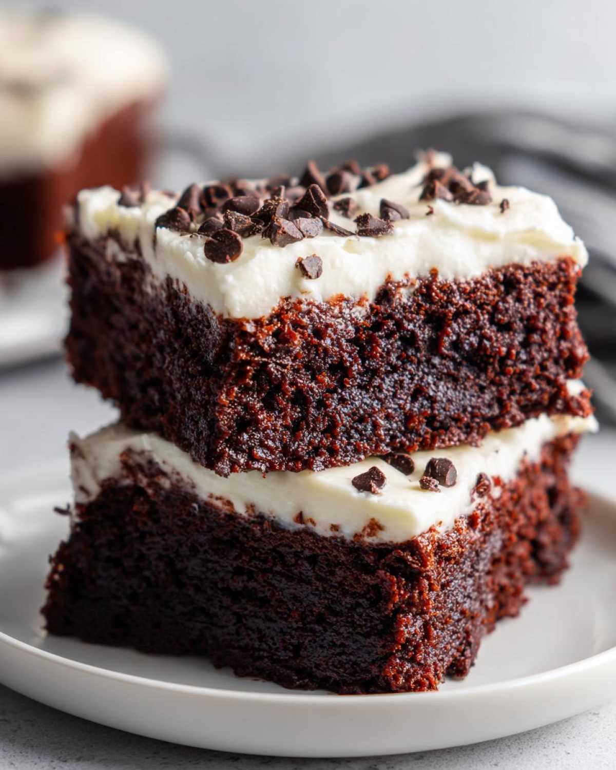 Two stacked slices of rich, dark gingerbread brownies topped with thick cream cheese frosting and mini chocolate chips.