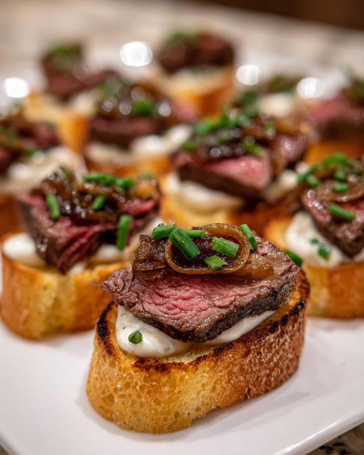 Close-up of a perfectly cooked steak crostini topped with rare steak, caramelized onions, and chives on a creamy base.