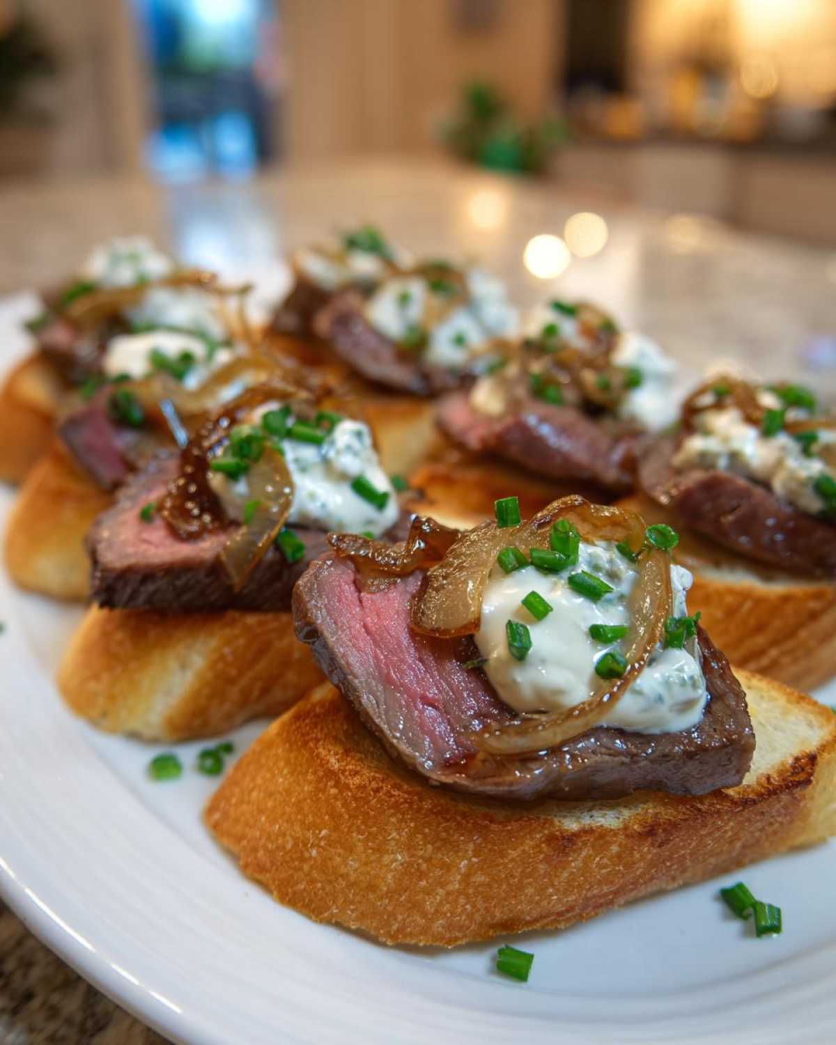 Close-up of several steak crostini appetizers topped with medium-rare steak, blue cheese sauce, and caramelized onions.