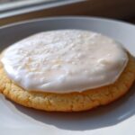 Close-up of a round sugar cookie topped with thick, white sugar cookie icing that hardens.