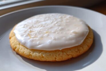 Close-up of a round sugar cookie topped with thick, white sugar cookie icing that hardens.