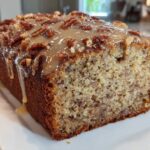 Close-up of a loaf of sweet alabama pecan bread topped with pecan halves and a thick caramel glaze dripping down the side.
