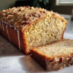 Close-up of a loaf of sweet alabama pecan bread, sliced, showing a thick pecan glaze dripping down the side.