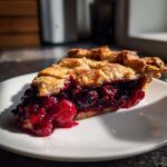 A close-up slice of triple berry pie showing a thick, juicy berry filling and flaky golden crust.