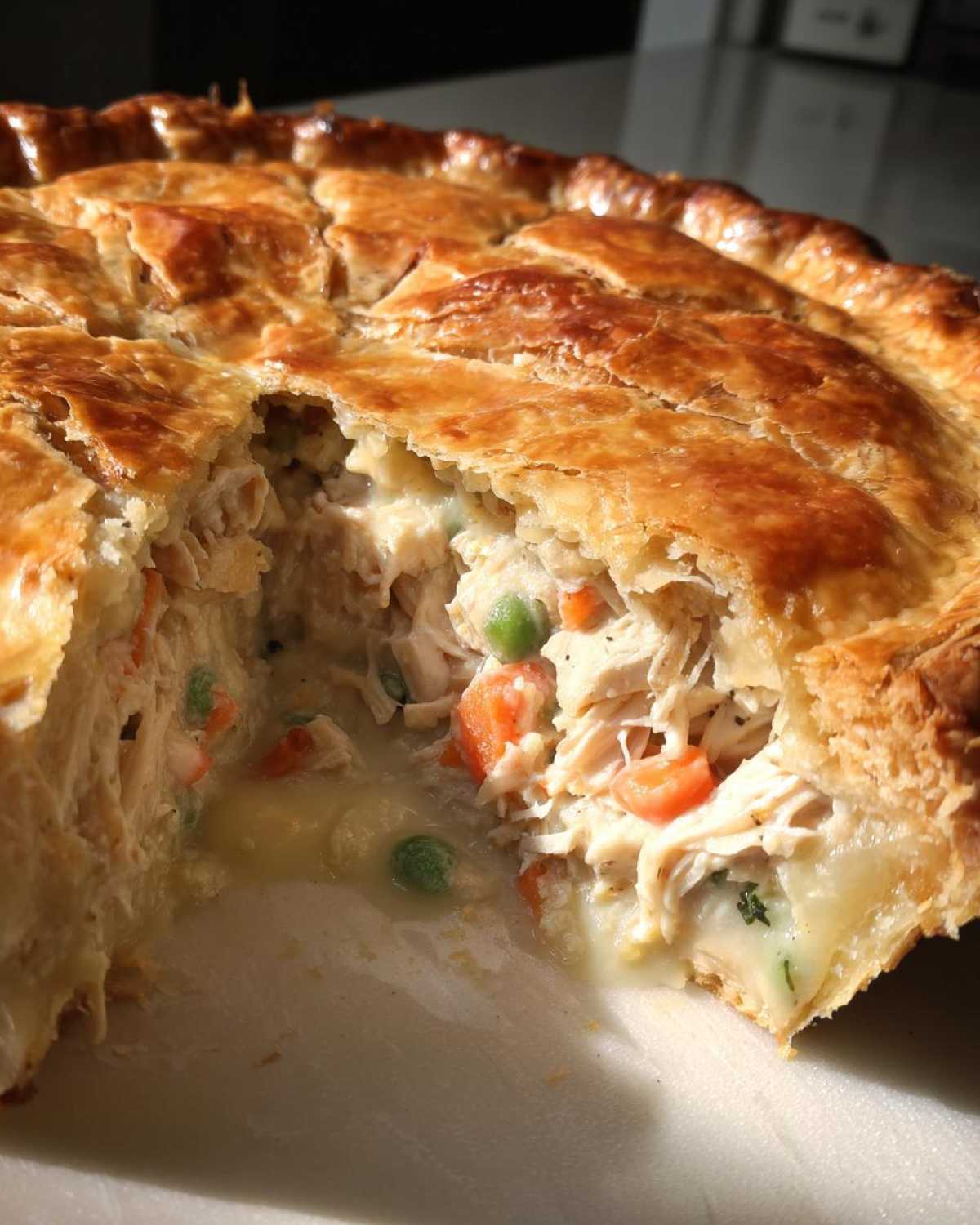 Close-up of a freshly baked turkey pot pie recipe with a golden, flaky crust broken open to show creamy filling, shredded turkey, peas, and carrots.