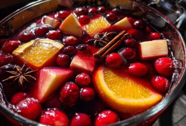 Close-up of vibrant holiday sangria floating with cranberries, orange slices, apple chunks, star anise, and cinnamon sticks.