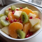Close-up of a vibrant winter fruit salad featuring kiwi, orange segments, apple chunks, and pomegranate seeds.