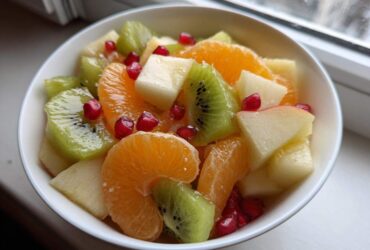 Close-up of a vibrant winter fruit salad featuring kiwi, orange segments, apple chunks, and pomegranate seeds.