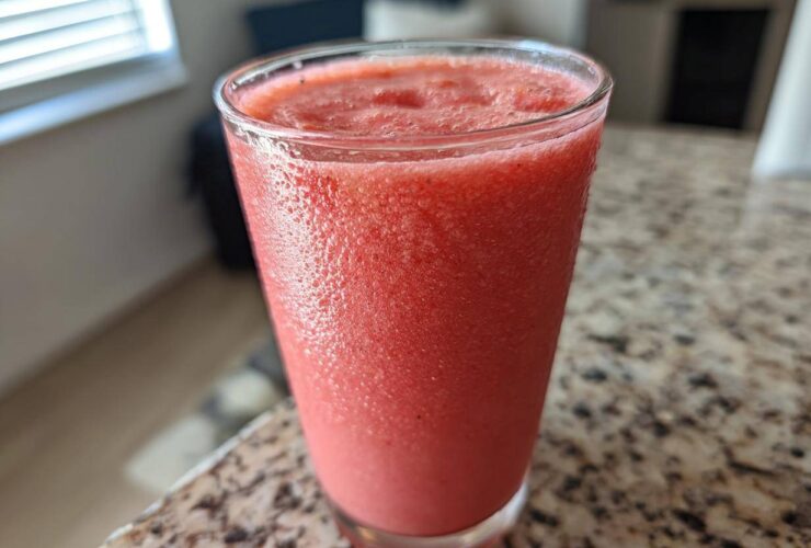 Close-up of a tall glass filled with a vibrant, frosty watermelon smoothie sitting on a granite countertop.