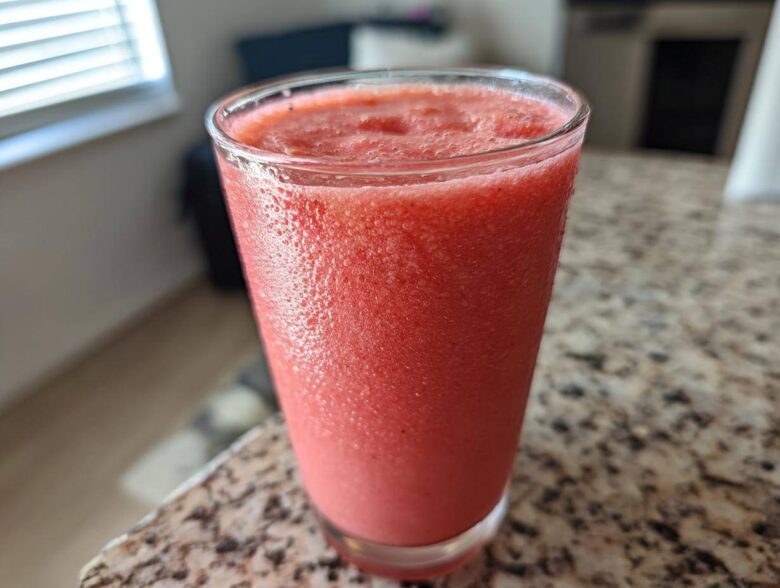 Close-up of a tall glass filled with a vibrant, frosty watermelon smoothie sitting on a granite countertop.