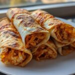 Close-up of several golden, crispy Air Fryer Crispy Buffalo Chicken Taquitos piled on a white plate.