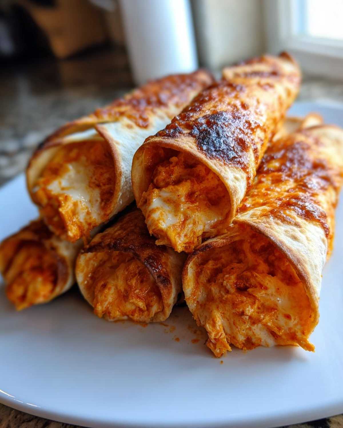 A stack of crispy Air Fryer Crispy Buffalo Chicken Taquitos showing melted cheese and orange buffalo sauce filling.