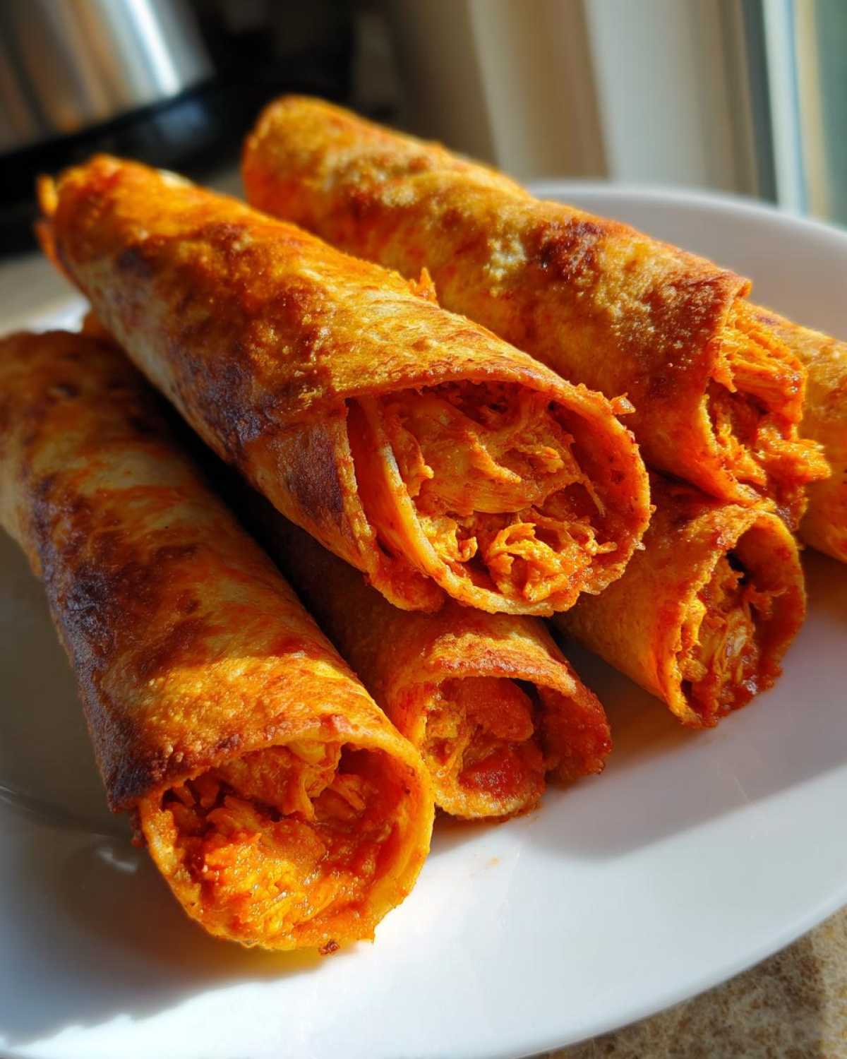 Close-up of golden-brown, crispy Air Fryer Buffalo Chicken Taquitos filled with shredded orange chicken filling.