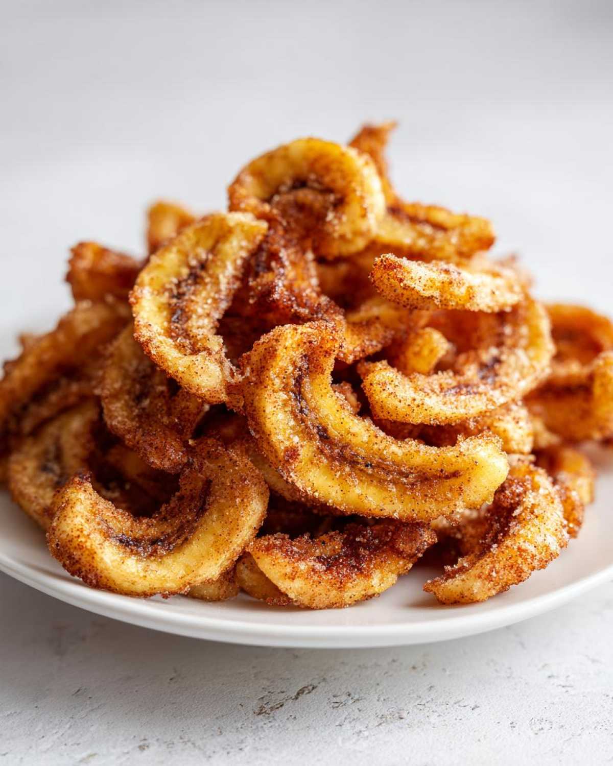A mound of Air Fryer Crispy Cinnamon Sugar Banana Chips piled high on a white plate.