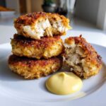 Close-up of three Air Fryer Crispy Crab Cakes stacked, one broken open showing flaky crab meat, served with a dollop of lemon aioli.
