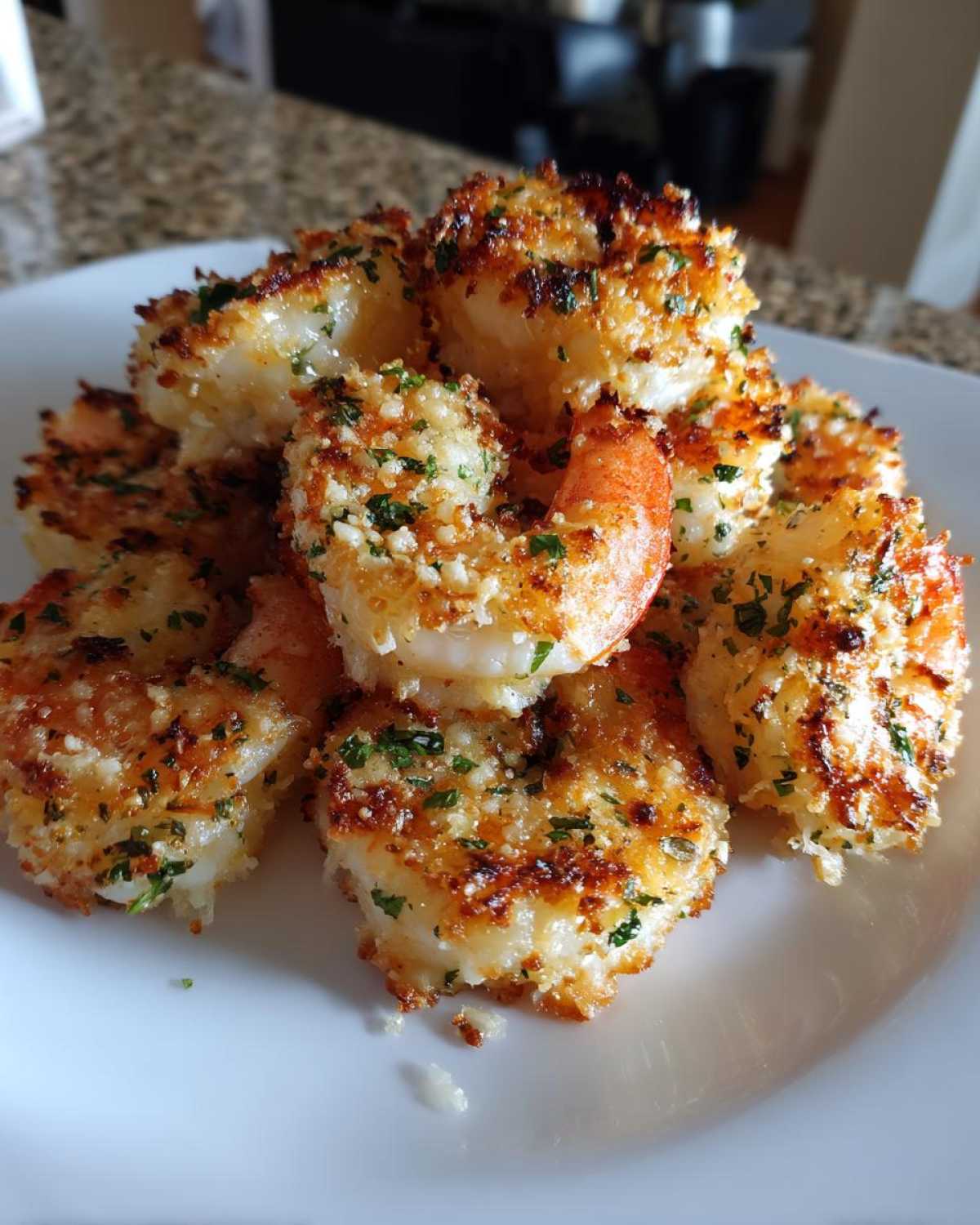 A close-up of several pieces of Air Fryer Crispy Garlic Parmesan Shrimp piled high on a white plate.