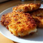 Close-up of three golden brown Air Fryer Crispy Parmesan Chicken Cutlets stacked on a white plate.