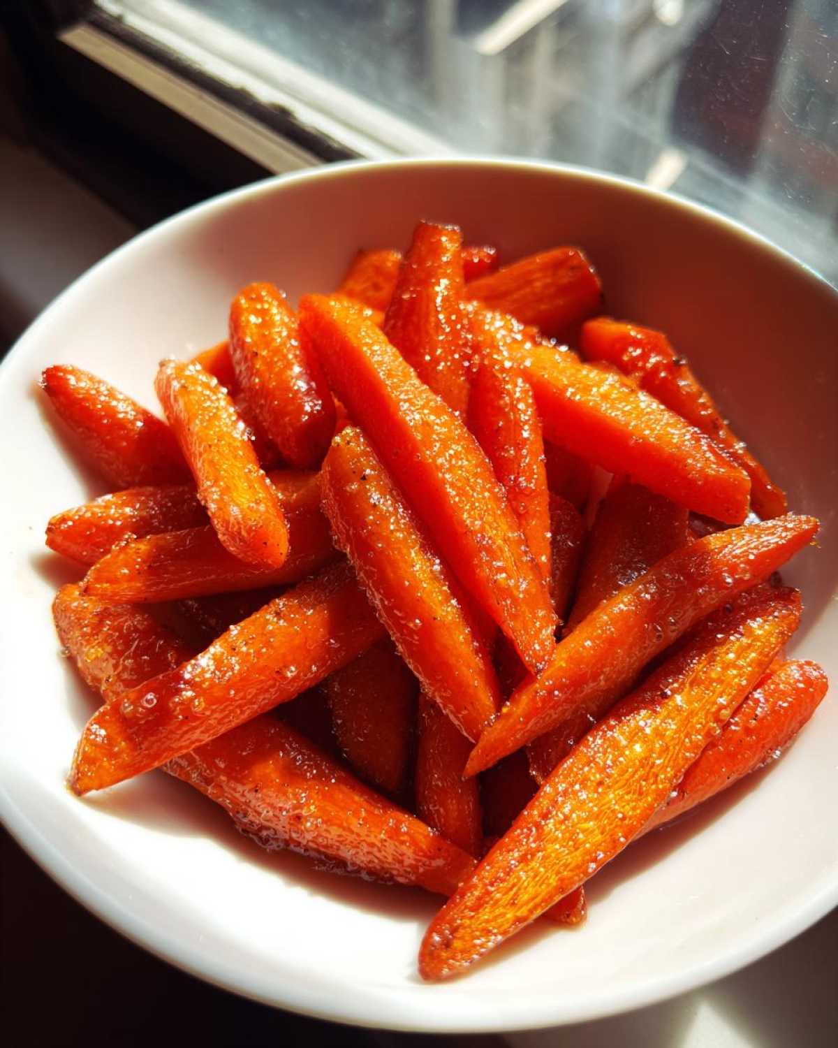 Close-up of bright orange Air Fryer Maple Glazed Carrots glistening with sweet glaze in a white bowl.