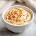 Close-up of creamy Copycat Outback Bloomin' Onion Sauce topped with red spice flakes in a white dipping bowl.