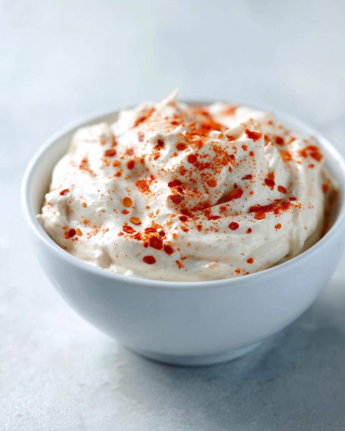 Close-up of creamy Copycat Outback Bloomin' Onion Sauce topped with red pepper flakes in a white bowl.
