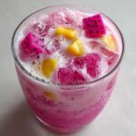 Close-up of a vibrant pink Copycat Starbucks Dragonfruit Refresher topped with ice and chunks of pink dragonfruit and mango.